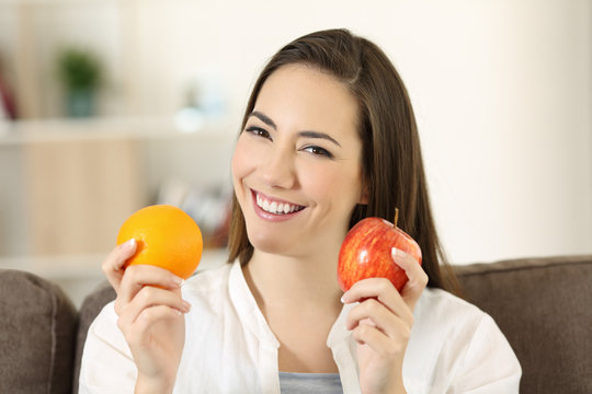 Woman holding an apple and orange looking at camera