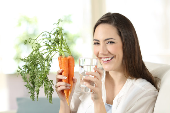 Woman holding carrots and a water glass looking at camera