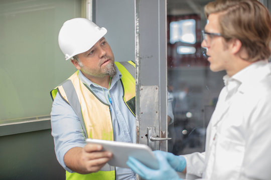 Workman and lab worker in thread factory, holding digital tablet