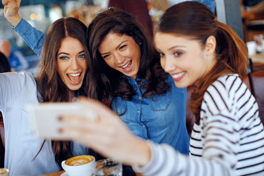 Three young happy women doing selfie in a cafe