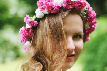 Beautiful girl in pink flower crown smiles you in summer park. Spring woman photo. International women's day and mother's day holidays. Flower chaplet. Pure sight. Young beauty portrait. Wavy hair.