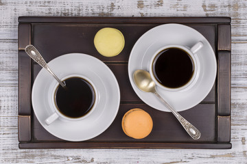 Two cups of coffee, spoon and macaron cakes on tray on white wooden table. Lifestyle concept. Close up