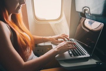 young red-haired woman uses laptop while flying on airplane near window, close-up