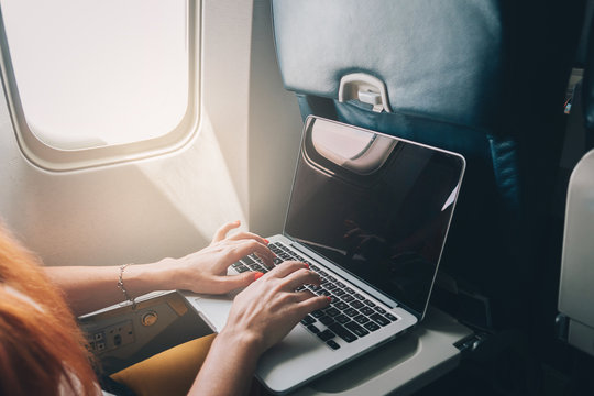 young red-haired woman uses laptop while flying on airplane near window, close-up