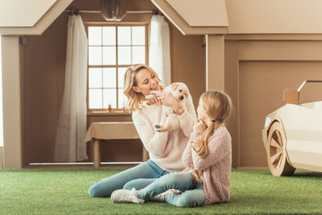 beautiful mother and daughter playing with adorable labrador puppy in front of cardboard house