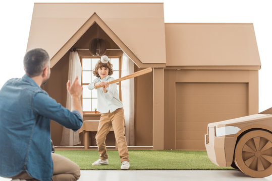 Father Teaching His Son How To Play Baseball In Front Of Cardboard House Isolated On White