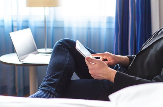 Business man reading news or email with tablet in hotel room. Businessman using smart mobile device and relaxing. Remote working online with modern technology.
