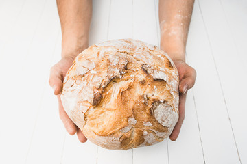 Closeup of male hands put fresh bread on an old rustic table on black background with copy space...