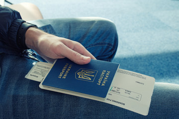 Young man in jeans holding in  hand foreign passport of Ukraine with airplane ticket attached to it.