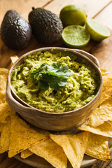 Bowl of guacamole dip with tortilla chips and ingredients in background