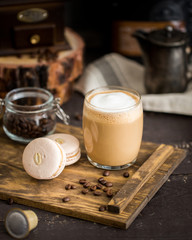 The perfect tasty breakfast!) The cup of latte or cappuccino coffee with milk and peanut, vanilla macarons on a wooden cutting board. Shadow background with beans, coffee grinder, capsule coffee.