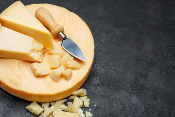 Head of parmesan or parmigiano hard cheese and pieces on concrete background