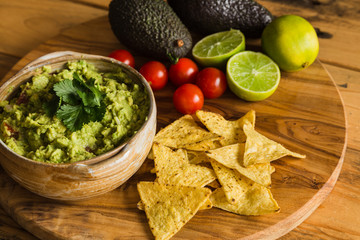 Bowl of guacamole dip with avocados tortilla chips cherry tomatoes and limes on a chopping board