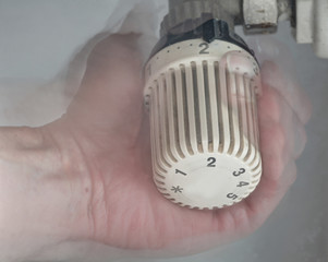 Hand stellt an einem Heizungsthermostat die Temperatur ein