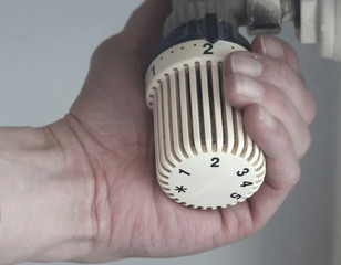 Hand stellt an einem Heizungsthermostat die Temperatur ein