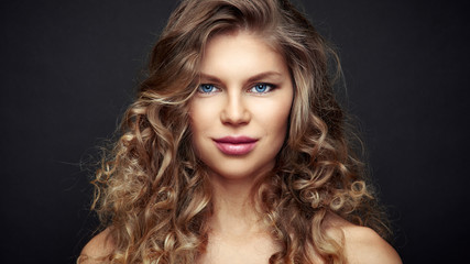 Fototapeta premium Studio portrait of young beautiful female with curly long hair over black background. 