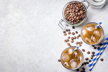 Vanilla iced coffee in glass and coffee beans in glass jar on white background. Top view, copy space.