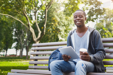 Obraz premium Smiling african-american student in the park with tablet oudoors