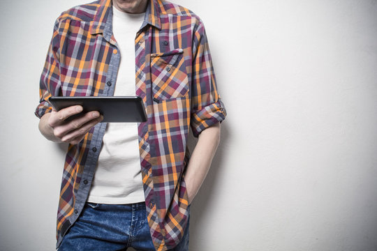 A young man holds a tablet in his hands. Hipster reads an e-book.