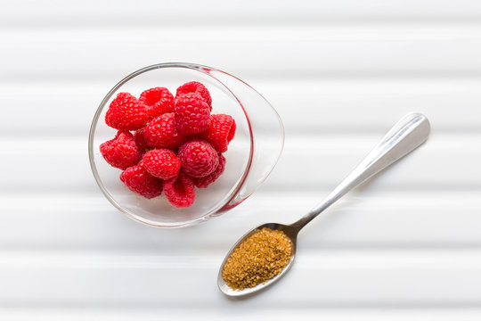 Close-up of isolated raspberries in bowl and brown sugar in spoon