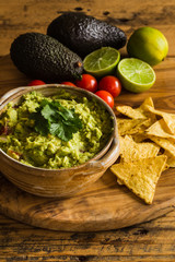 Guacamole dip in a bowl with scattered tortilla chips tomatoes avocados and limes