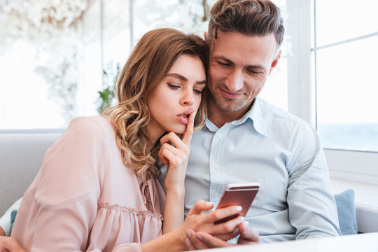Close up photo of lovely couple man and woman, resting and taking pleasure, while relaxing together in restaurant and using smartphone