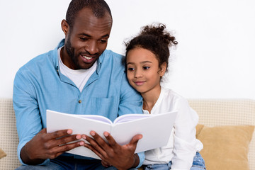 Obraz premium happy african american father reading book to daughter