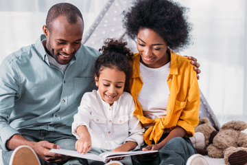 happy african american daughter reading for parents at home