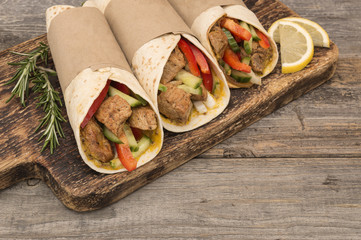 Fresh tortilla wraps with pork meat and fresh vegetables on wooden board. 