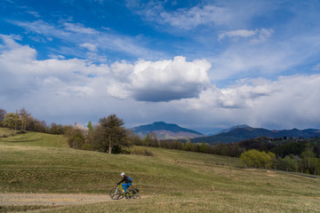 Fototapeta na wymiar Woman cyclist in a beautiful spring landscape in the Carpathian Mountains, Transylvania, Romania with clouds and a blue sky