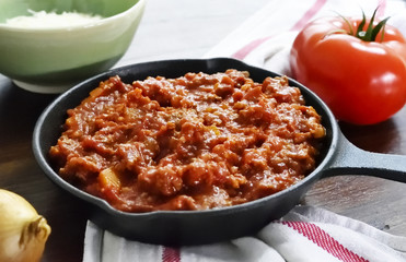 Bolognese sauce with parmesan cheese in a cooking pan or iron pan. Italian cuisine background with pasta sauce and slate plate.