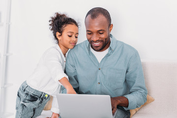 african american daughter showing something on laptop to father at home