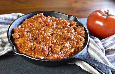 Bolognese sauce in a cooking pan or iron pan. Italian cuisine background with pasta sauce and slate plate.