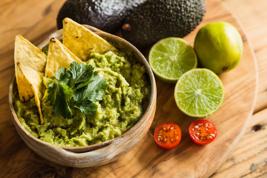 Tortilla chips in a bowl of guacamole dip with avocado limes and cherry tomato ingredients