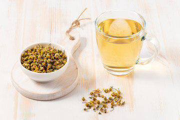 Cup of chamomile tea with dry chamomile flowers  on white wooden background.