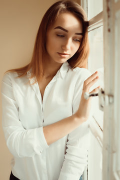 Closeup shot of lovely brunette lady in white shirt standing at the window