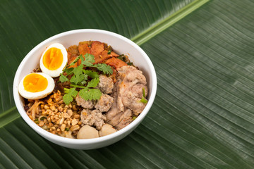 Spicy noodle soup with pork and egg in bowl on banana leaf