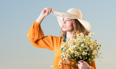 Summer look of a beautiful young woman in hat and red dress with a bouquet of daisies