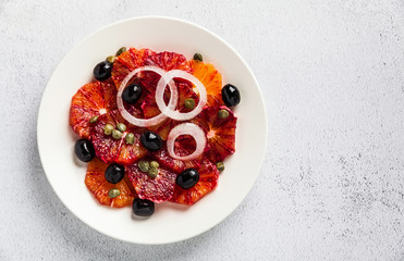 typical Spanish-style salad of red orange, onion and olives with capers and fresh raw olive oil and lime juice . Served on a stone white table. summer healthy snack or light lunch