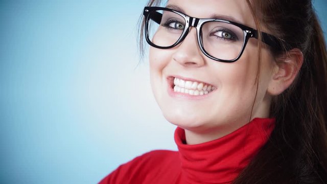 Attractive brunette woman wearing glasses looking at camera and smiling, blue background, copy space 4K ProRes HQ codec