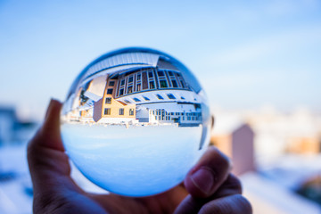 A hand holding a crystal ball for optical illusion. City as the background. Known as an orbuculum, is a crystal or glass ball and common fortune telling object. Performance of clairvoyance and scrying