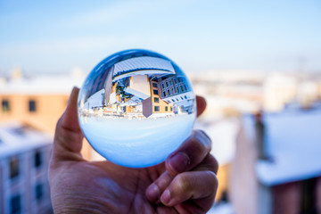 A hand holding a crystal ball for optical illusion. City as the background. Known as an orbuculum, is a crystal or glass ball and common fortune telling object. Performance of clairvoyance and scrying