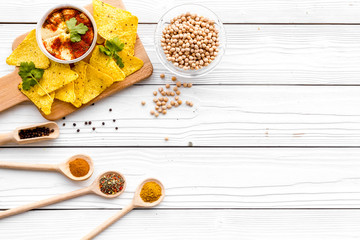 Serve hummus. Bowl with dish near pieces of crispbread on white wooden background top view copy space