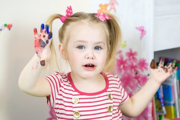 Cute girl shows dissapointment and sad emotions due to covered with paint hands and fingers