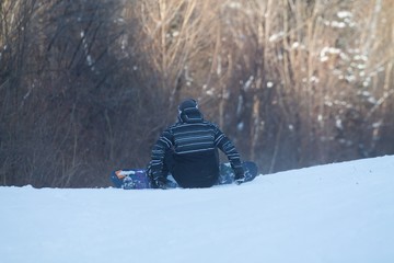 a snowboarder sitting on the snow in mountains and looking at the forest