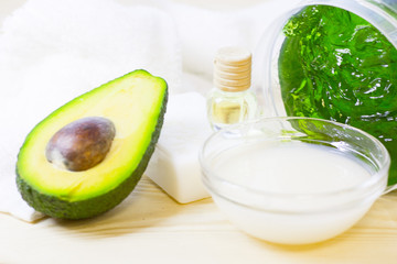 Avocado oil skin and hair care home spa. Avocado cut and jar of mask, a towel and a candle. White board background. Closeup