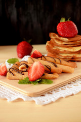 Golden crepes piled on a wooden board surrounded by fresh strawberries