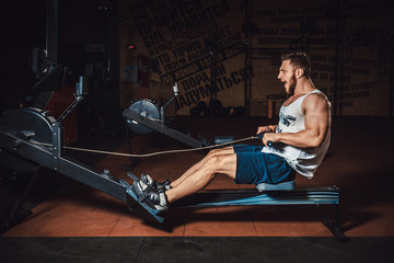Fitness young man using rowing machine in the gym and screaming © Oleksandr