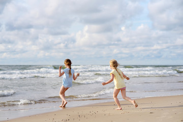 Fototapeta na wymiar Two little sisters having fun on a sandy beach on warm and sunny summer day. Kids playing by the ocean.