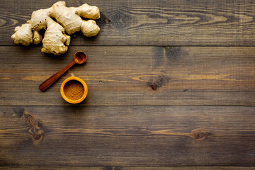 Spice and condiment. Ground ginger in small bowl near ginger root on dark wooden background top view copy space